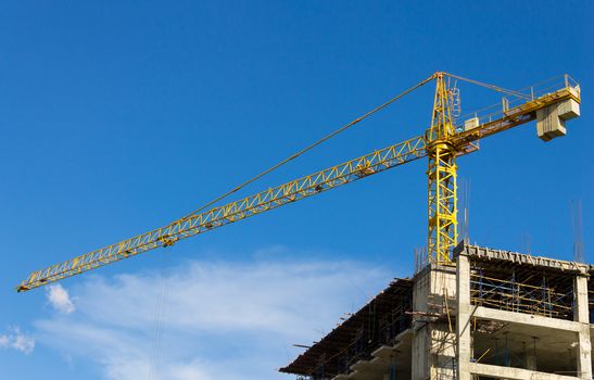 Yellow tower crane on blue sky background. Crane is building skyscraper in site.