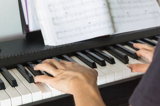 Hand of Piano Player on White Keys and Black Keys of Electric Piano with Piano Staff or Sheet Music