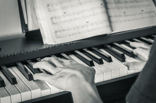 Hand of Piano Player on White Keys and Black Keys of Electric Piano with Piano Staff or Sheet Music