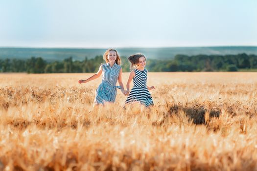 Happy teenage girls running down wheat field at the sunset