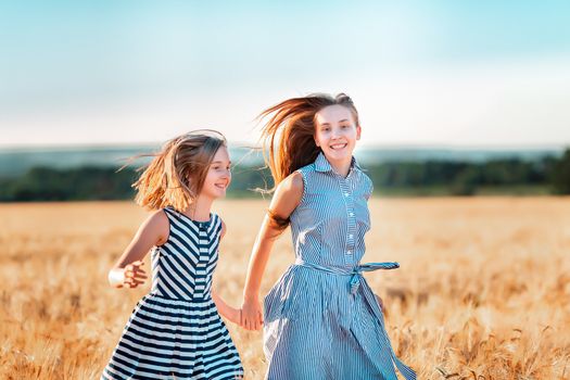 Happy teenage girls running down wheat field at the sunset