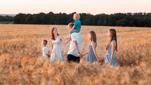 Happy big family walking down golden wheat field at the sunset. Family values concept