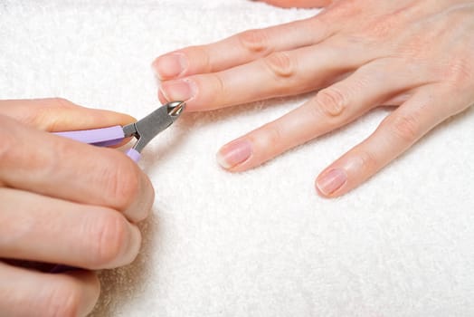 Woman's hand removing nail cuticle on light white table. Care about dry, overgrown cuticle. Closeup