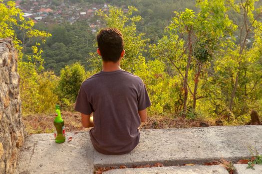 Enjoying drinking beer and looking at distant seascape on a vacation. An Indonesian teenagers looks at the landscape and drinks beer.