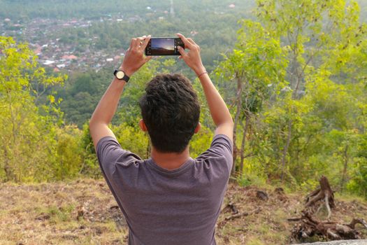 Man photographed mountains in the smartphone. A young man takes pictures of a volcano with a mobile phone. Indonesian teenager photographs during sunset.