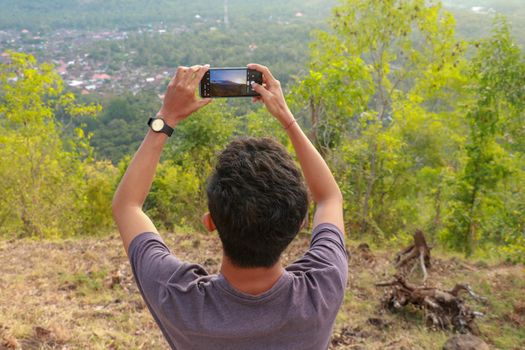 Man photographed mountains in the smartphone. A young man takes pictures of a volcano with a mobile phone. Indonesian teenager photographs during sunset.