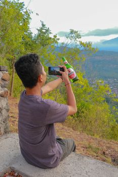 People and technology concept - close up of hands with smartphone picturing beer in nature. A young man takes pictures with a bottle of beer on his mobile phone.