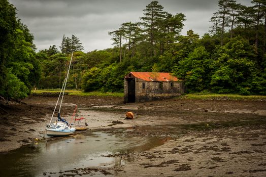 Two boats lie in a muddy river bed not too far from an apparently abandoned building.