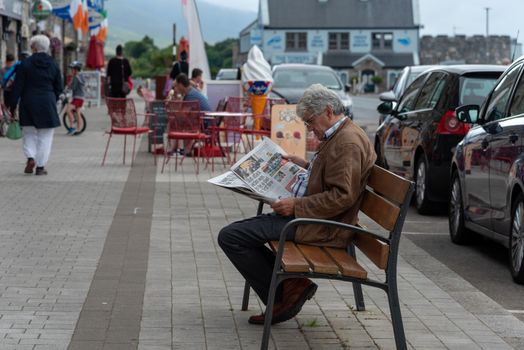Westport, Ireland -- July 14, 2018. A man sits on a bench reading a newspaper in town.