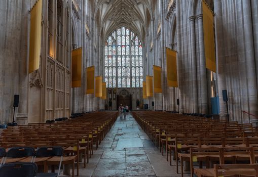 Winchester, England -- July 17, 2018. A wide angle photo taken inside Windsor Cathedral showing stained glass windows and art work in the Church. Tourists are in the center aisle at the back of the Church.
