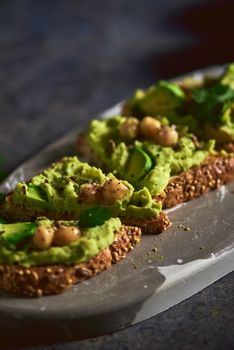 Toast of avocado hummus, decorated with chickpeas on stone table