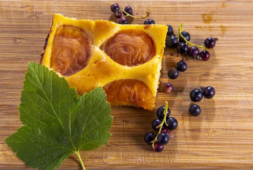 Cake with apricot and blackcurrant decorated with currant leaves on a wooden board