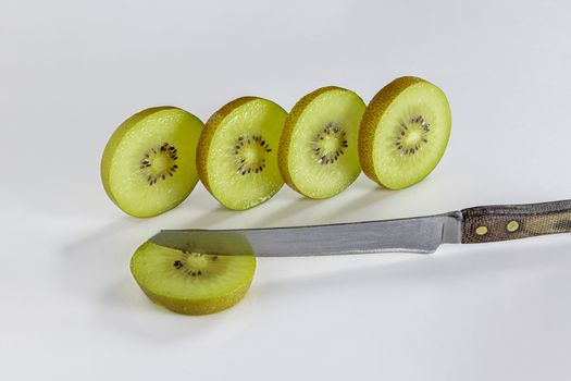 

Four thin slices of kiwi sliced stand against a white background and a knife lies near