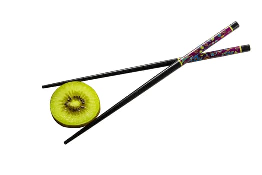 One thin slice of Kiwi sliced lies against a white background and is held by two crossed Chinese sticks