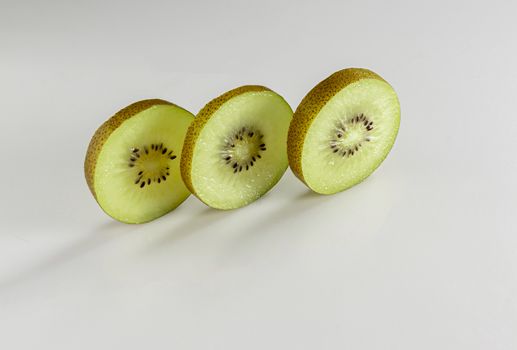 Three thin slices of kiwi sliced stand against a white background