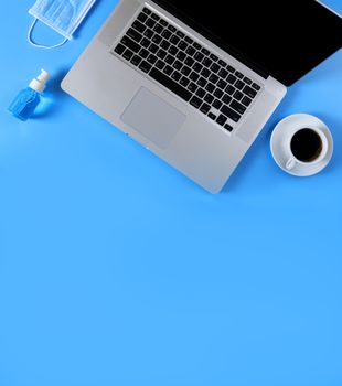 Work from home concept. Top view Laptop, black coffee., medical face mask, Blue alcohol hand sanitizer gel on blue background with copy space banner.