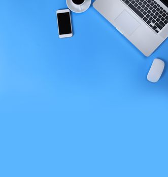 Top view laptop, mouse, smart phone and coffee on blue background. Laptop, mouse, mobile phone, black coffee isolated on blue background with copy space banner. Business concept.