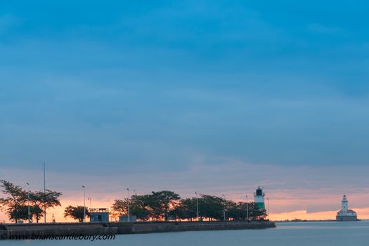 Golden glow of sunset on horizon beyond Chicago Harbor Lighthouse and beacon under dark blue sky and breakwater.