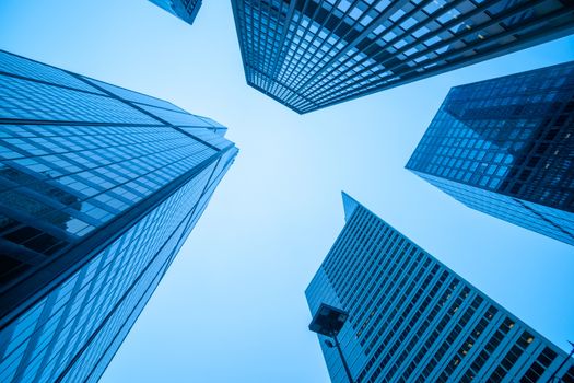 Converging high-rise commercial office buildings in blue hues towering skyward from street level.