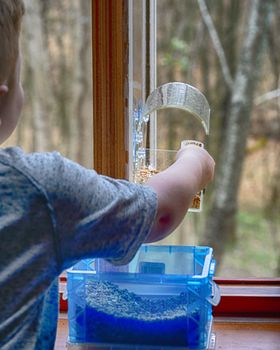 Small boy loads window-mounted bird feeder with seed.