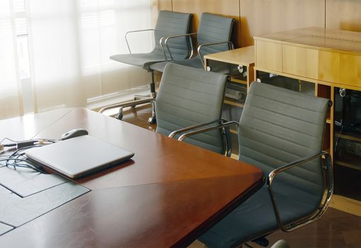 a laptop closed on the wooden table of a corporate board with some empty chairs. Business and management