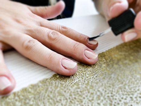 Hands of a female applying transparent nail polish on the nails with a black brush. Manicure and personal care