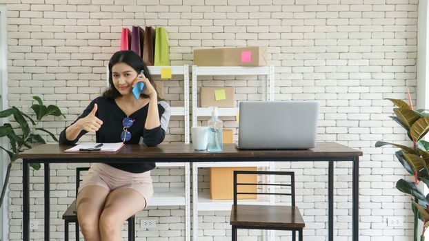 Merchant A young, modern Asian woman has a career selling online. Talking on the phone, receiving orders from customers and notes. She uses communications technology and the internet to market