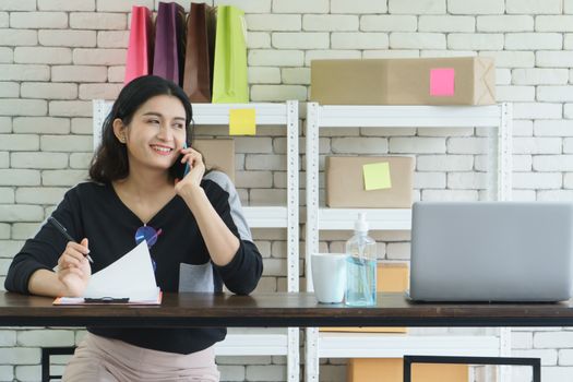 Entrepreneurs in the online sales business, attractive young Asian women carrying mobile phones and checking customers from computers. Merchant business owner Small size, marketing using technology