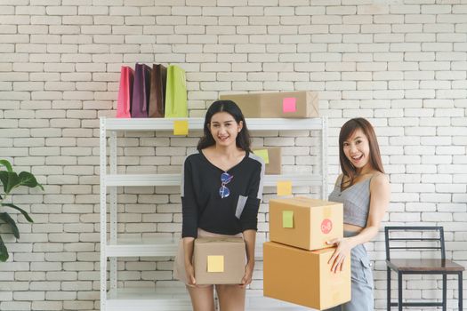 Merchant Two attractive young Asian women make living selling products online. They are checking the boxes to send customers. They use communication technology and the internet to market