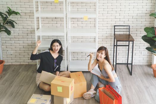 Merchant Two attractive young Asian women make living selling products online. They are checking the boxes to send customers. They use communication technology and the internet to market