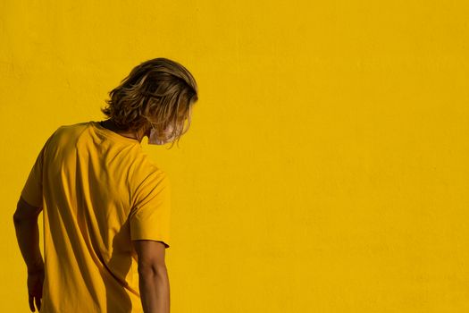 Blond young man with mask on a yellow background. Summer coronavirus concept