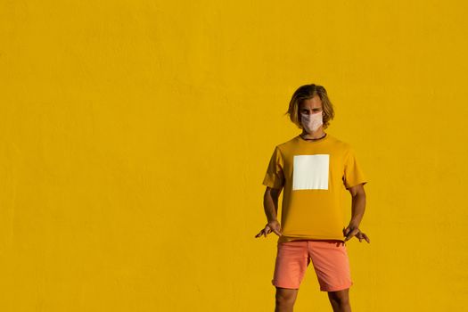 Blond young man with mask on a yellow background. Summer coronavirus concept