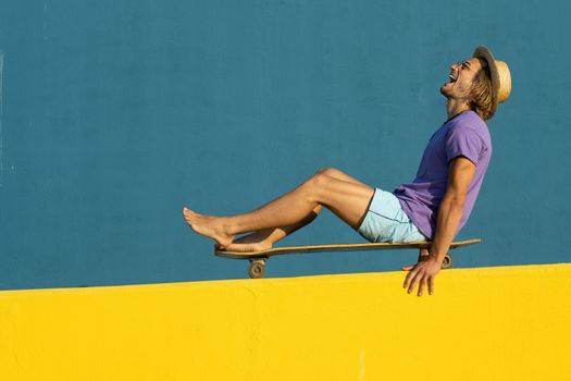 Blond young man with skateboard, hat and sunglasses enjoying the summer