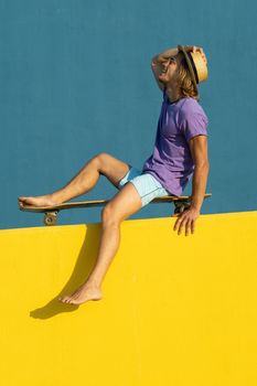 Blond young man with skateboard, hat and sunglasses enjoying the summer