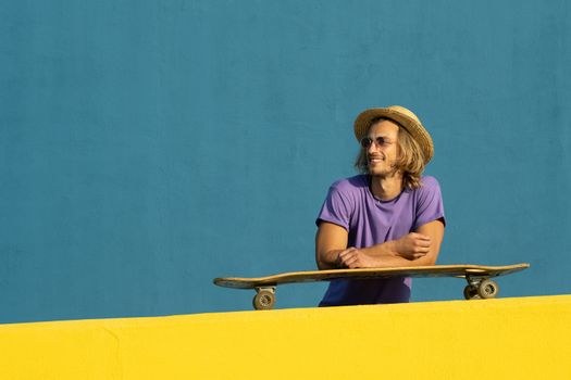 Blond young man with skateboard, hat and sunglasses enjoying the summer