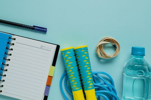 Notebooks with measure tape, fresh drinking water, jump rope on blue background for healthy diet taking notes concept