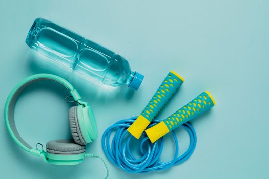 Fresh drinking water, jump rope and headphones on blue background for sports and healthcare concept