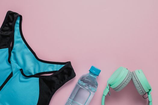 Sport bra for exercise, fresh drinking water and headphones on pink background for sports and healthcare concept