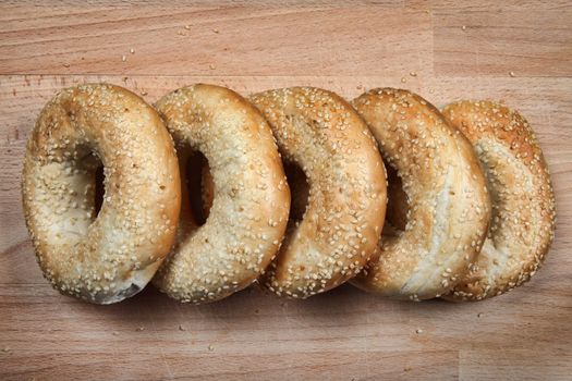 Sesame seeded bagel bread rolls on a wooden chopping board