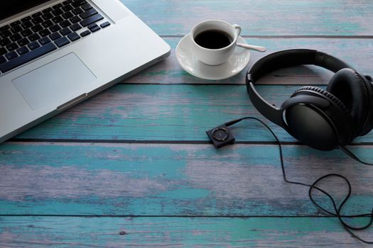 Laptop, Headphone, Music player, black coffee on blue wood table. With copy space. Business concept.