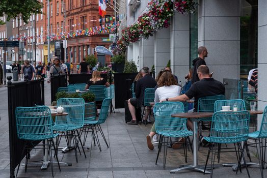 Dublin, Ireland -- July 9, 2018. People sitting at an outdoor cafe in Dublin, Ireland having coffee while nearby pedestrians walk past.