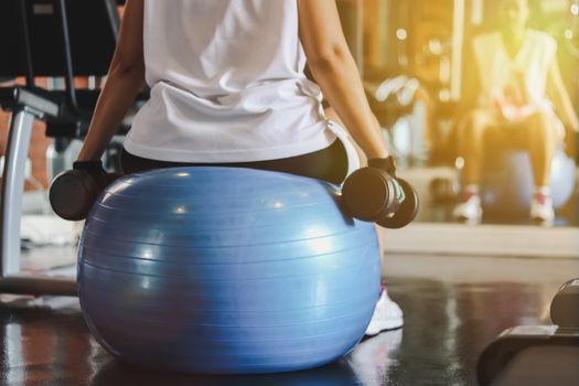 woman working out with dumbbells sitting on gymnastic ball.