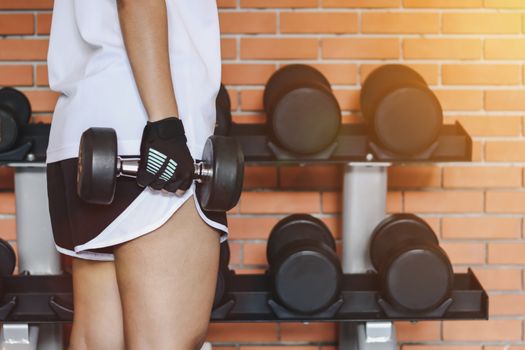 Close up woman are lifting dumbbells in the fitness room with dumbbells on rack.