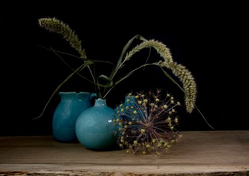 still life with three blue vases, ears of corn and a flower of an onion bulb on a dark background with light from the right side