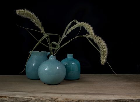 still life with three blue vases, ears of corn  on a dark background with light from the right side
