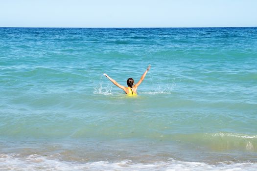 girl with hands up in the sea, rear view, copy space