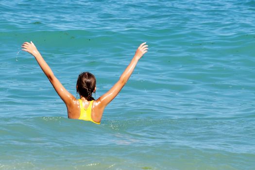 girl with hands up in the sea, rear view, copy space