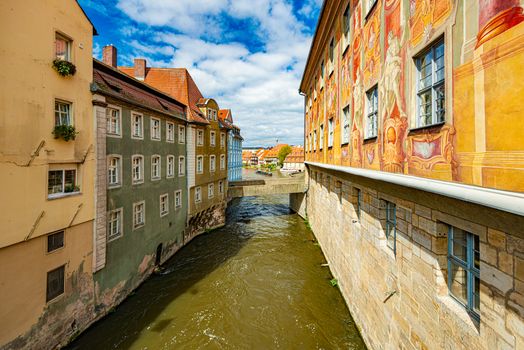 Old city in Germany. Travel in Europe. Beautiful street architecture. Town of Bamberg. Canal with water in foreground and blue cloudy sky in background.