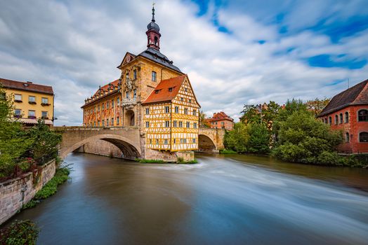 Bamberg city in Germany. Town hall building in background with blue cloudy sky.  Architecture and travel in Europe. Flowing river in foreground.