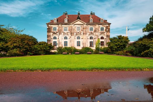 Old house with green lawn in Dresden, Germany. Water puddle with reflection in foreground and blue cloudy sky in background